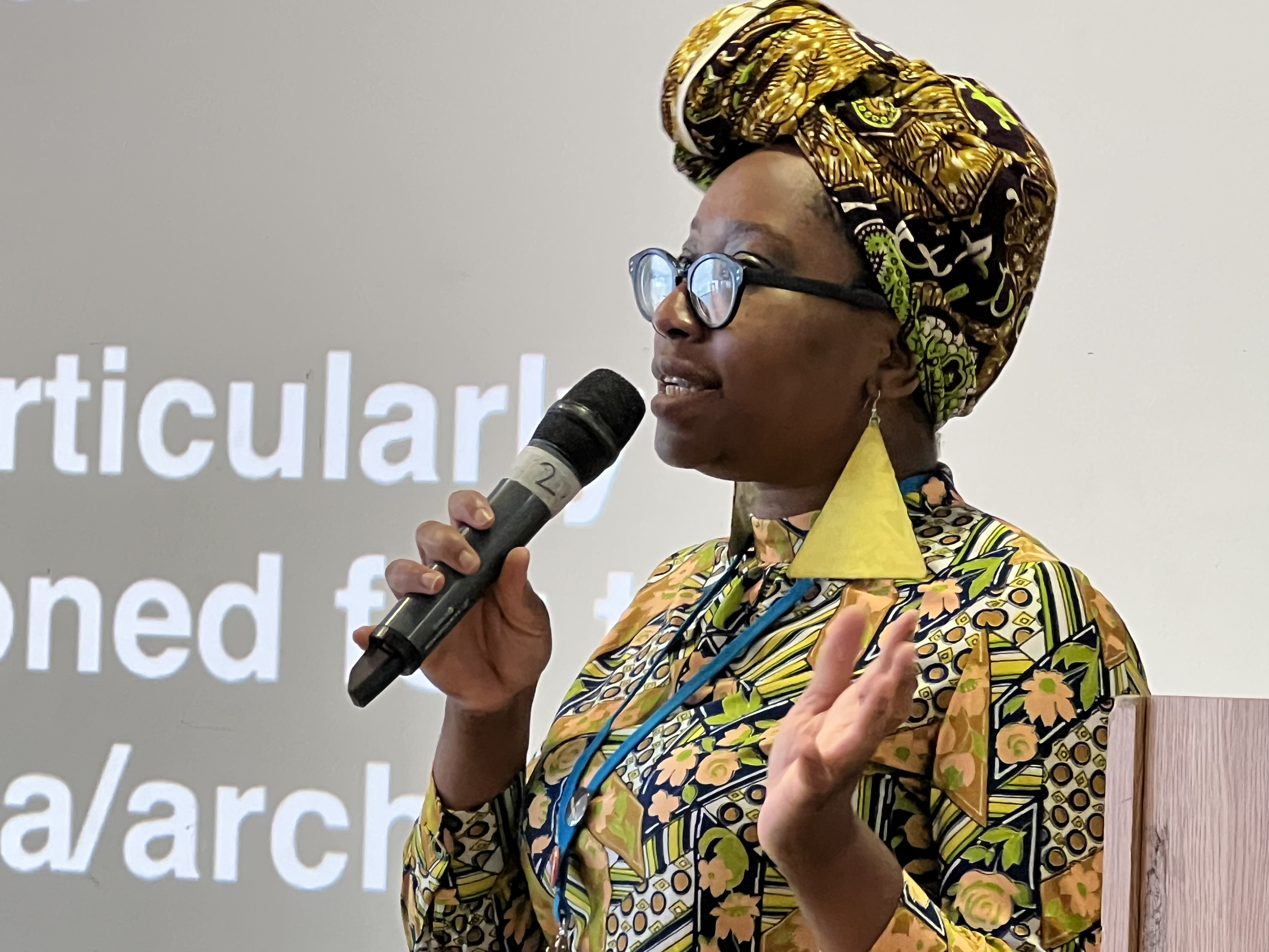 Florence Okoye holding a microphone whilst she presents at UXBristol in front of her slides