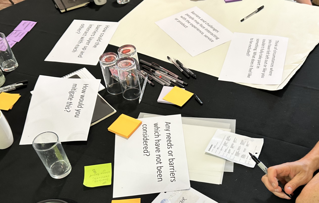 Table with pens, post it notes, glasses and question prompts printed on pieces of paper