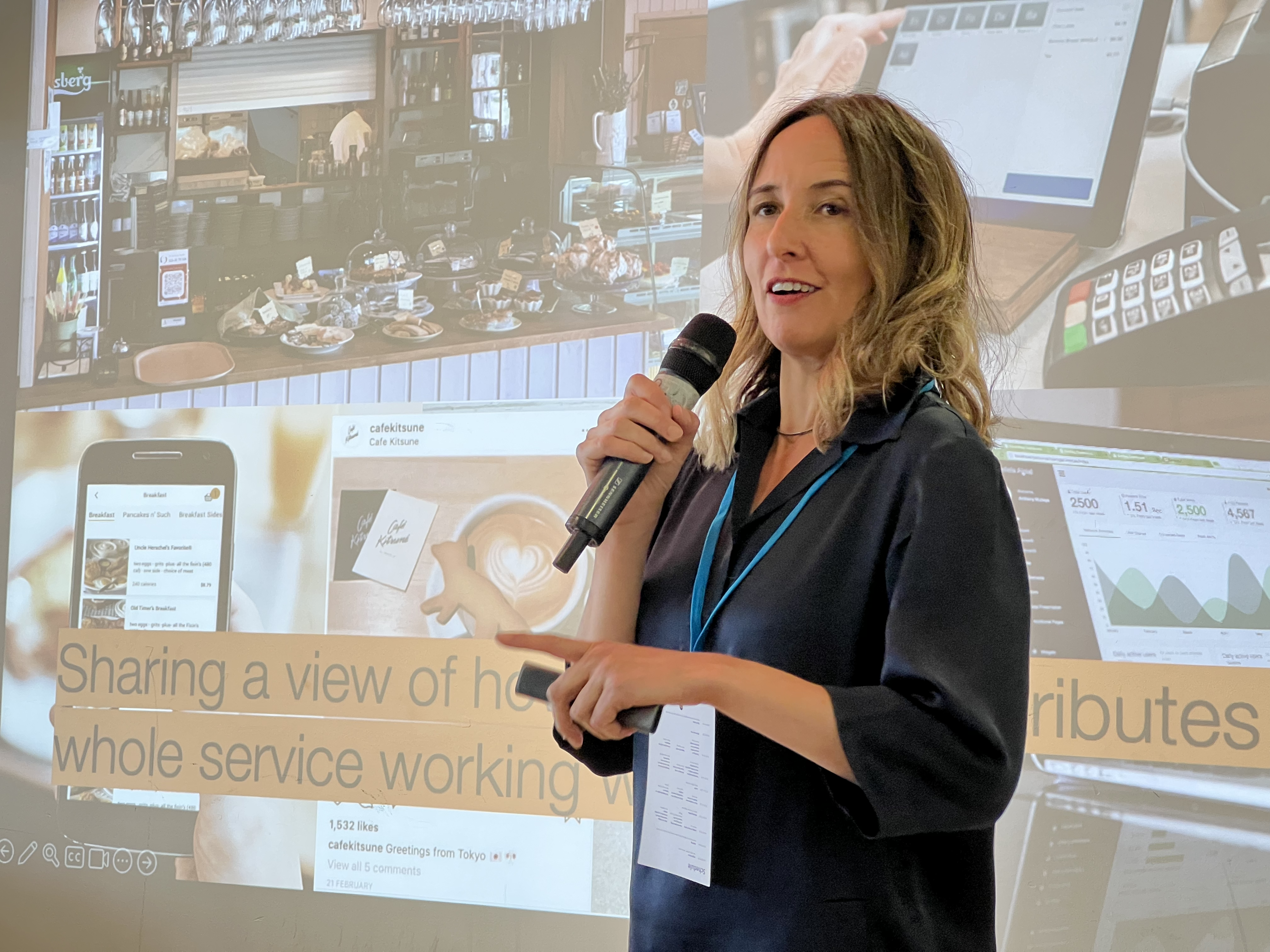 Kate Tarling holding a microphone and presenting in front of a projector screen at UXBristol